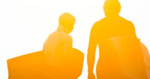 a silhouette of a man and woman holding surfboards