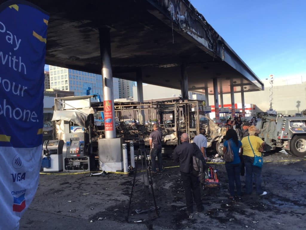 a group of people standing around a burned out gas station